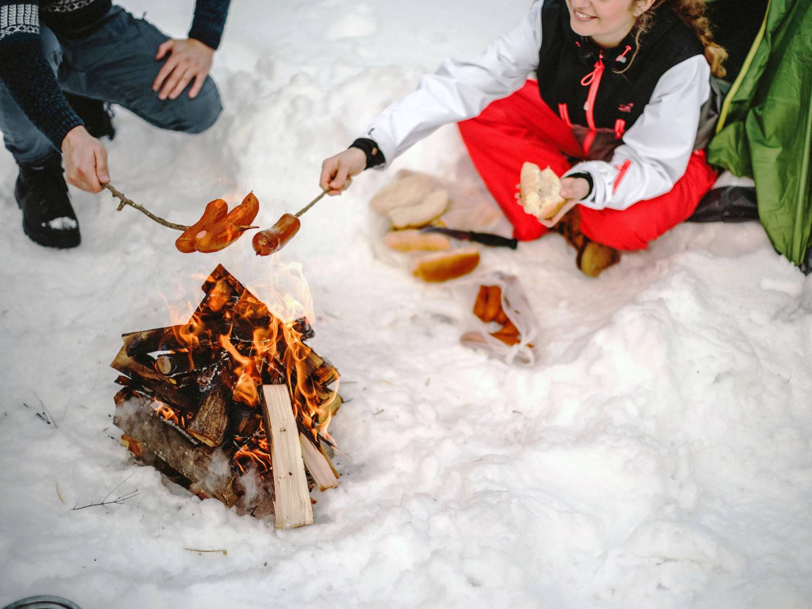 To personer griller pølser over et bål i snøen under en tur i naturen.
