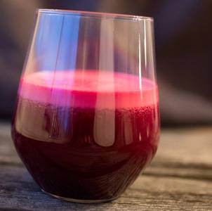 Et glass med rødbetjuice eller smoothie med en dyp rød farge, plassert på et trebord.