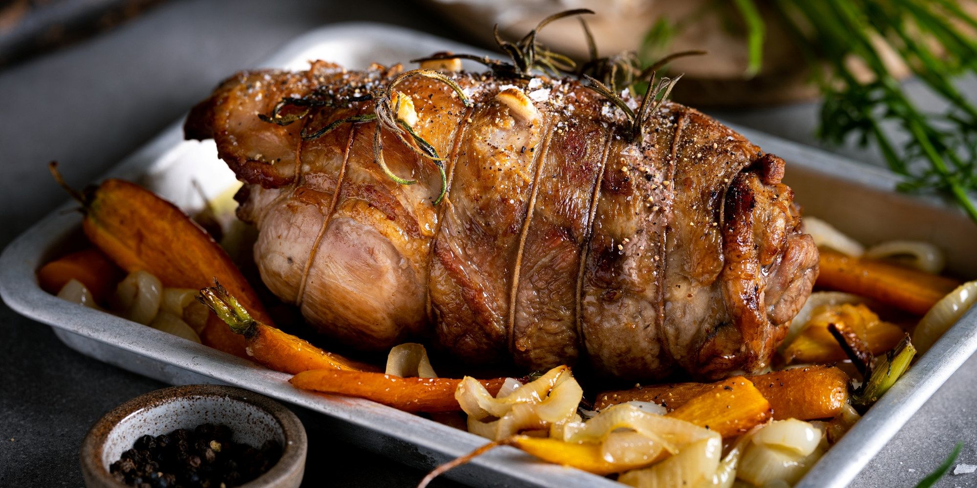 En klassisk lammestek servert med ovnsstekte gulrøtter og hvitløk på et serveringsfat.