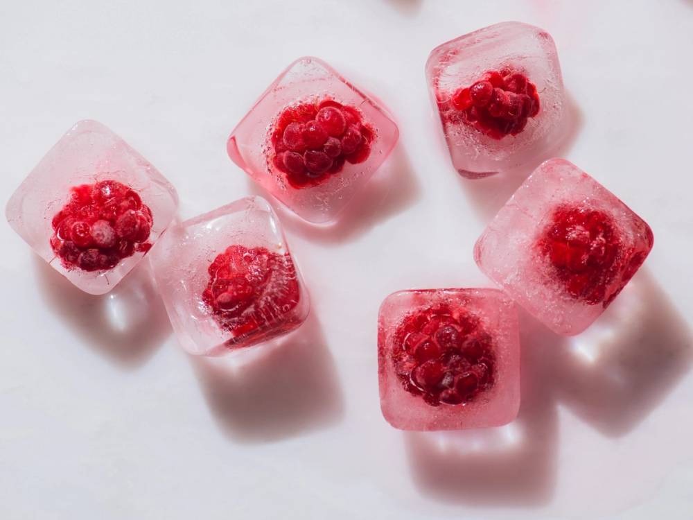 Ferske isbiter med bringebær inni, plassert på en hvit bakgrunn.