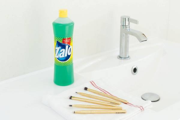 En flaske Zalo vaskemiddel står ved en vask på badet, med bomullspinner og en rød og hvit stripet tråd på vasken.