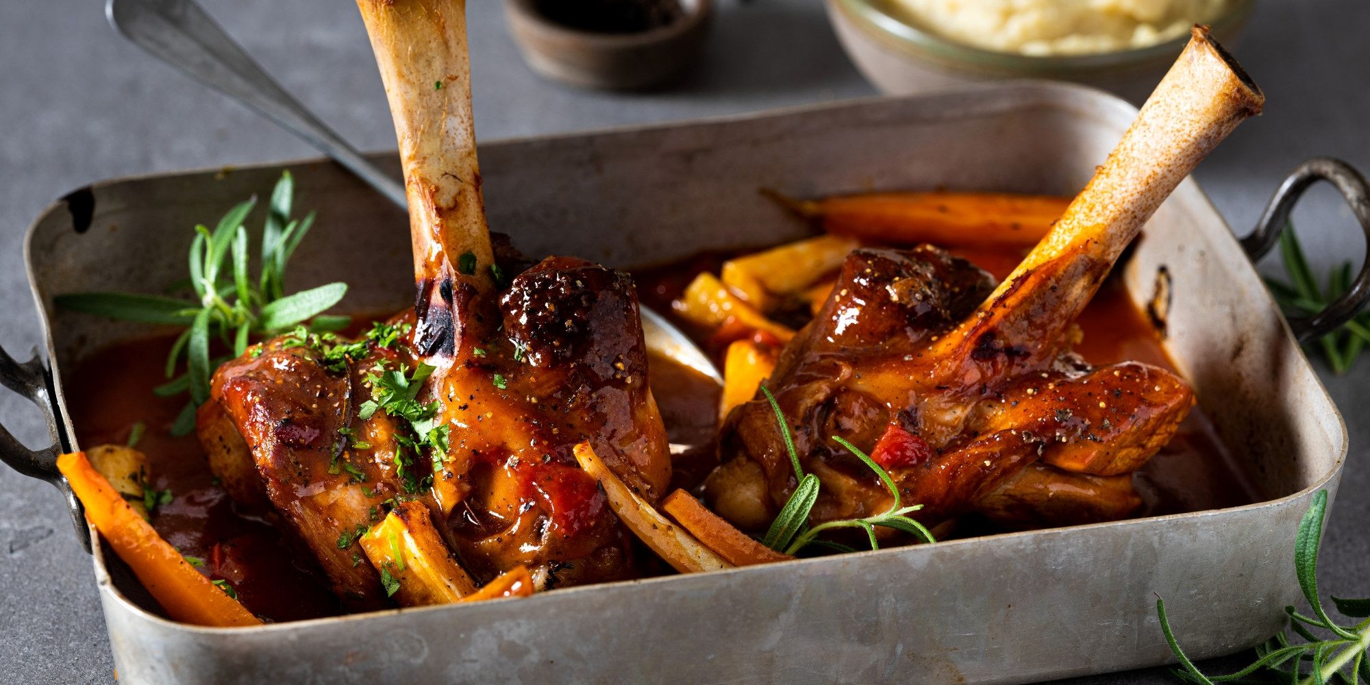 Lammestek med rotgrønnsaker i en ildfast form, pyntet med friske urter.