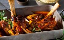 Lammestek med rotgrønnsaker i en ildfast form, pyntet med friske urter.