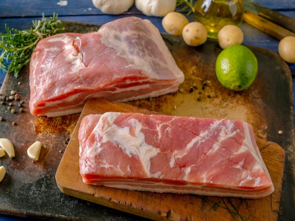 To stykker rått kjøtt på skjærebrett med urter, sitron og hvitløk rundt.