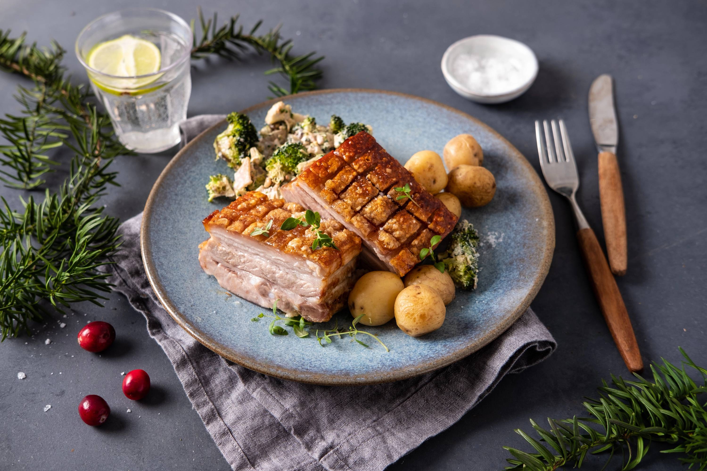 Ribbe med brokkolisalat og små poteter på en blå tallerken, omgitt av julepynt og bestikk.