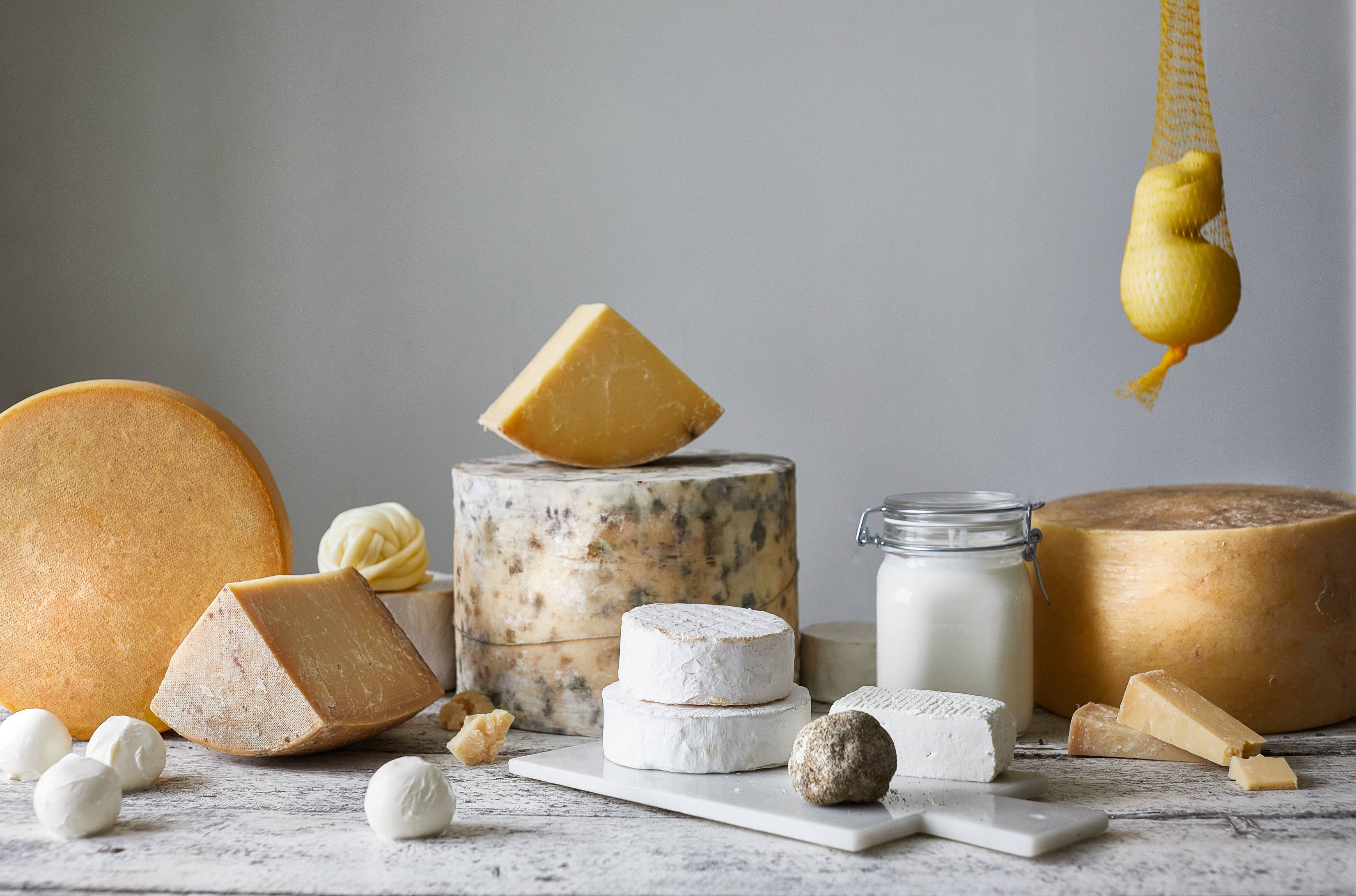 Et ostebord med ulike typer ost, kjeks og en liten skål med noe hvitt, plassert på et bord mot en lys bakgrunn.