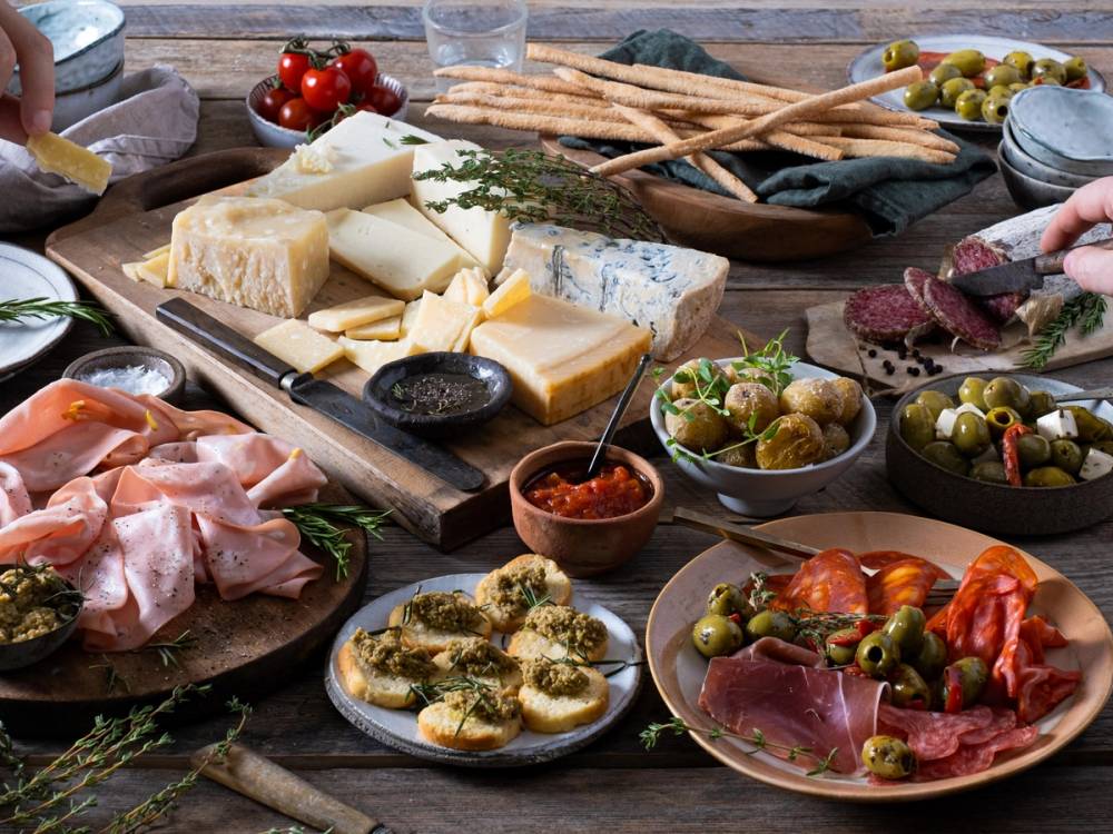 Et utvalg av spekemat, ost, oliven og brød på et bord, klar til å serveres som en del av en spekematmeny.