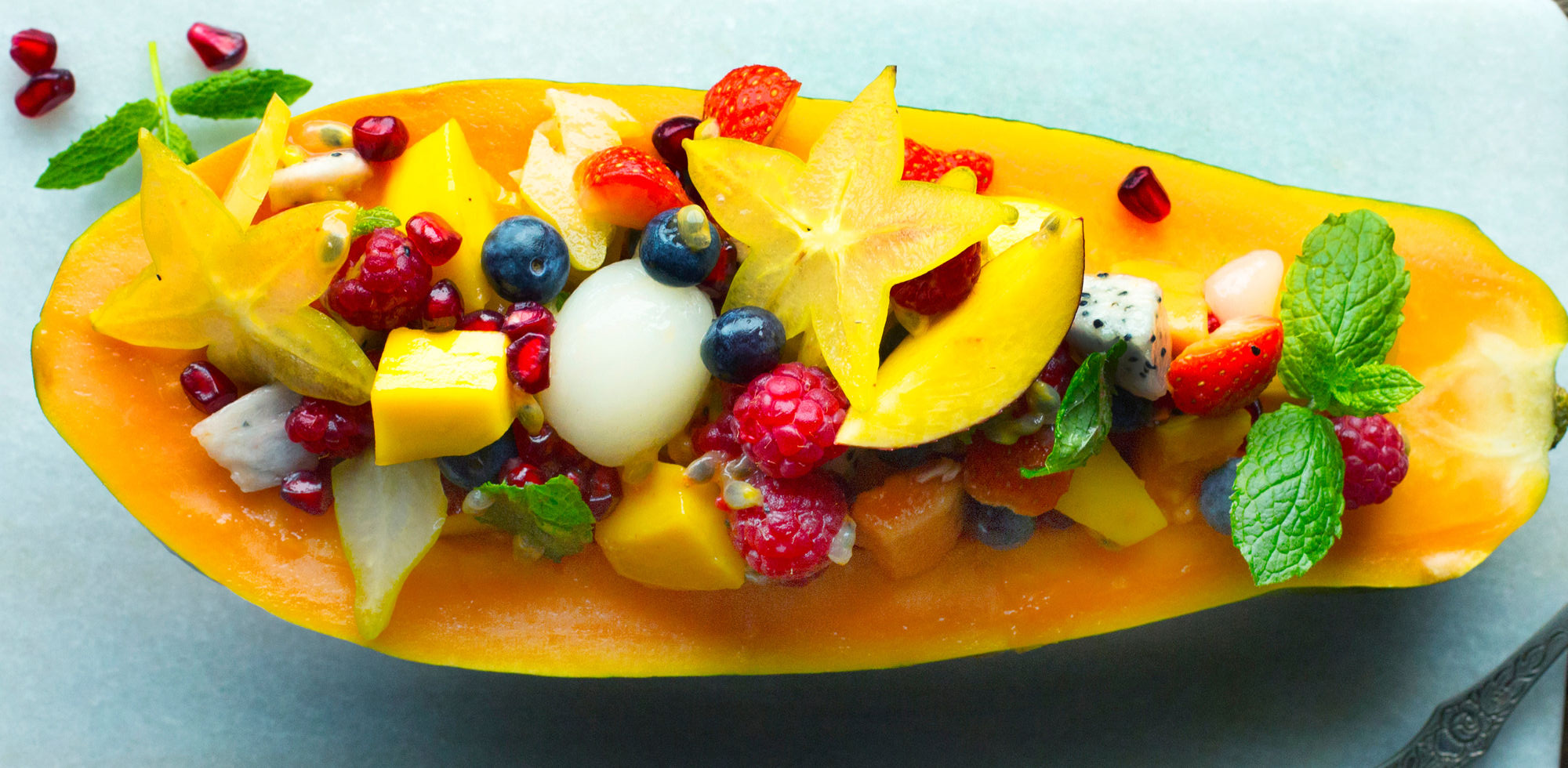 Eksotisk frukt med mango, druer, bær og mynte på en tallerken, klar til å spises.