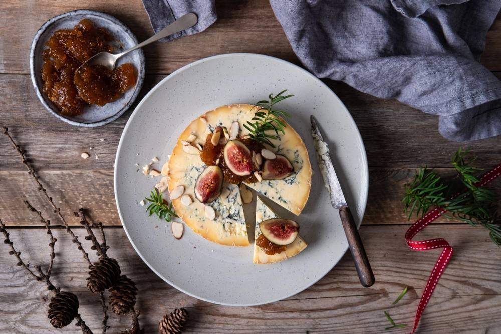 En ostetallerken med fikenmarmelade og frukt, omgitt av julepynt og et glass med marmelade, på et trebord.