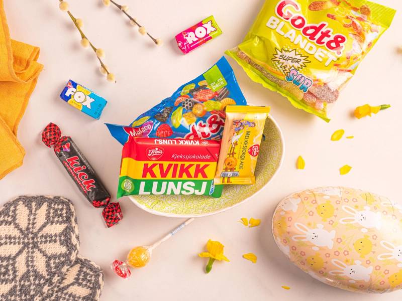 Ulike typer smågodt og godteribiter i en skål, omgitt av påskeegg og pynt på et hvitt bord.