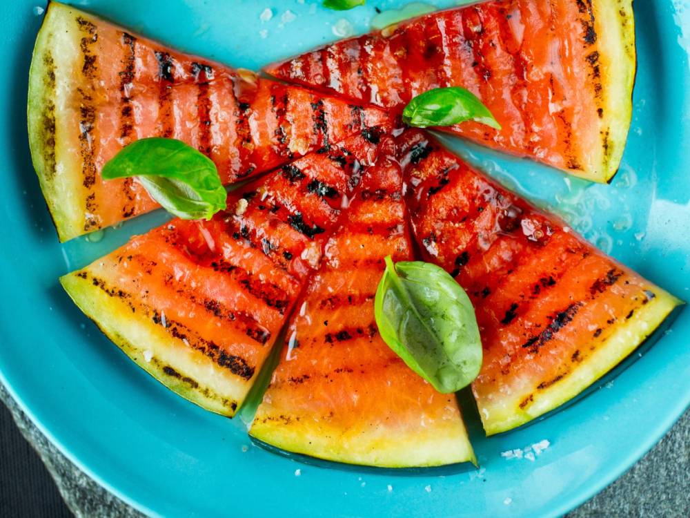 Vannmelon skåret i biter og grillet med grillmerker, pyntet med basilikumblader på en blå tallerken