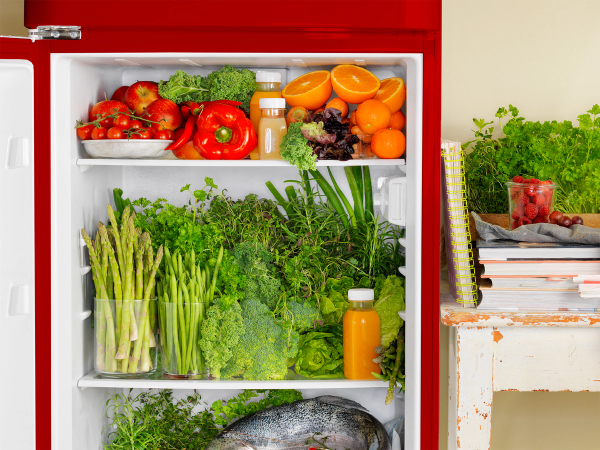 Friskt grønnsaker og frukt i et kjøleskap, med en liten plante og noen bøker på bordet ved siden av.