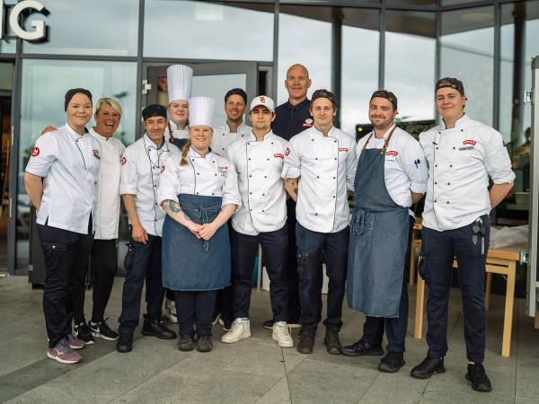 En gruppe kokker og en leder står sammen under generalprøve for NM i Sjømat 2022 i et moderne rom med store vinduer.