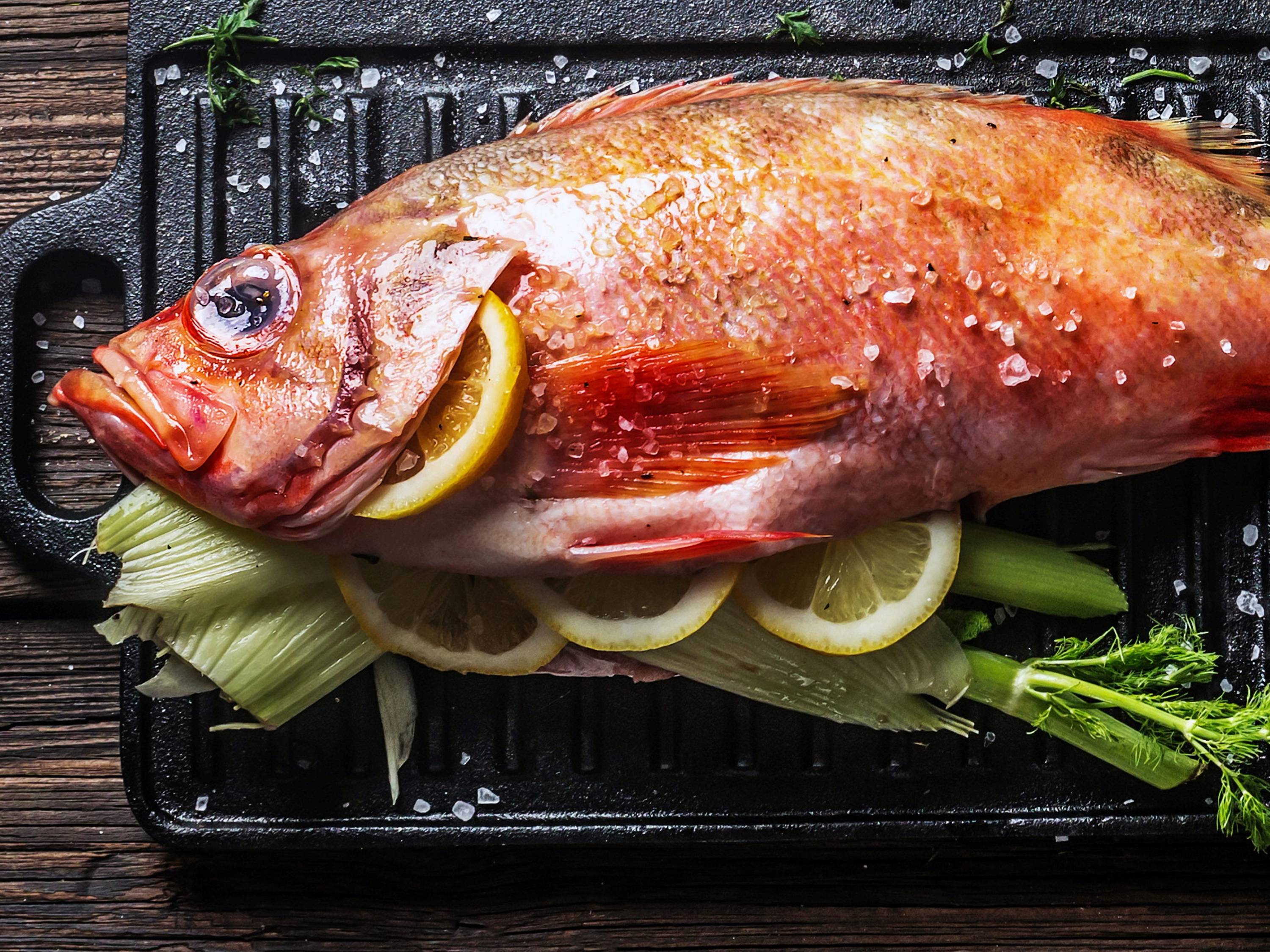Uer som ligger på en svart grillplate med sitronskiver og grønnsaker rundt.