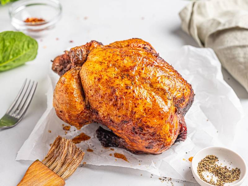 Nygrillet kylling med sprø skorpe ligger på hvitt papir, omgitt av krydder og grønnsaker.