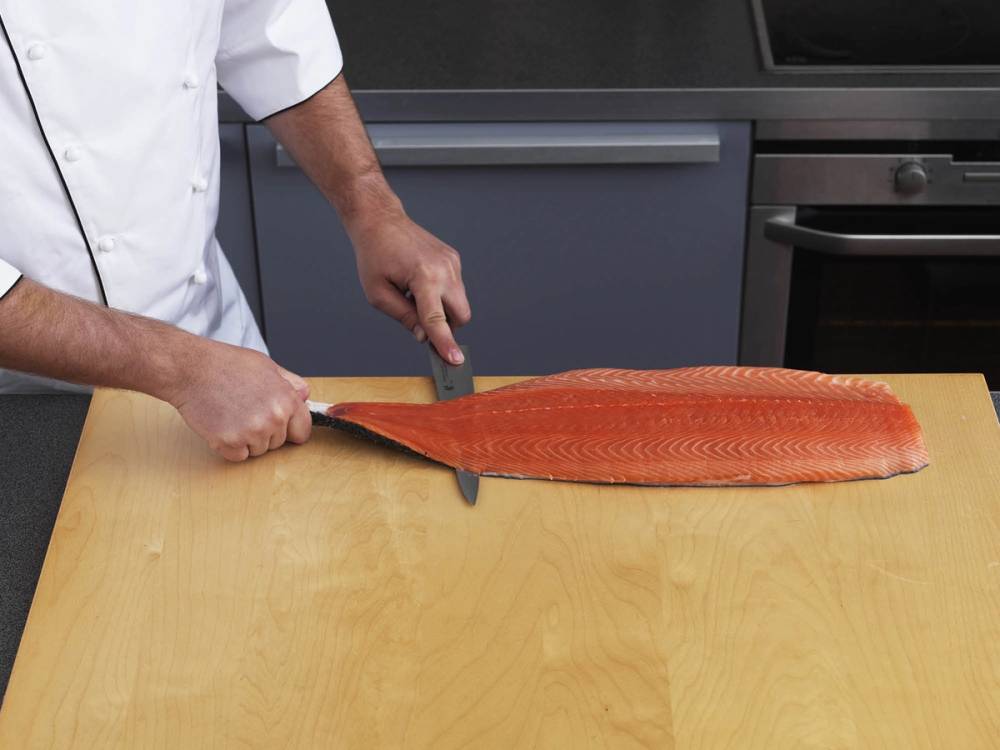 Person som fileterer en hel laks på kjøkkenbenken.