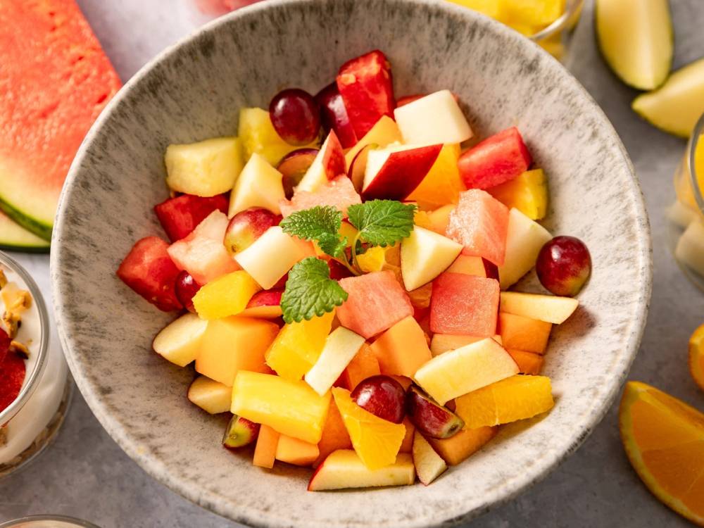 Fargerikt fruktbeger med ulike biter av melon, vannmelon, druer og annen frukt i en grå skål.