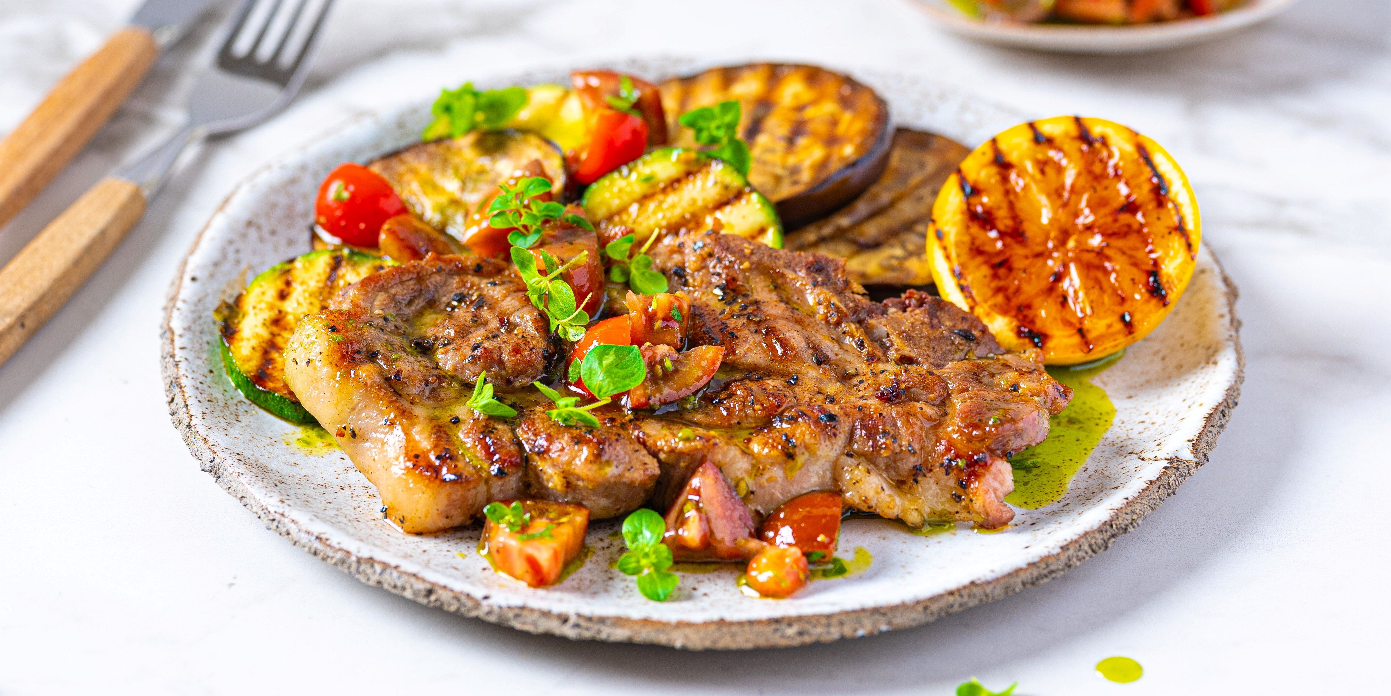 Marinert nakkekotelett med grillede grønnsaker og potet, ser ut til å være servert på en tallerken.