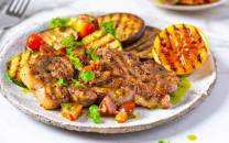 Marinert nakkekotelett med grillede grønnsaker og potet, ser ut til å være servert på en tallerken.