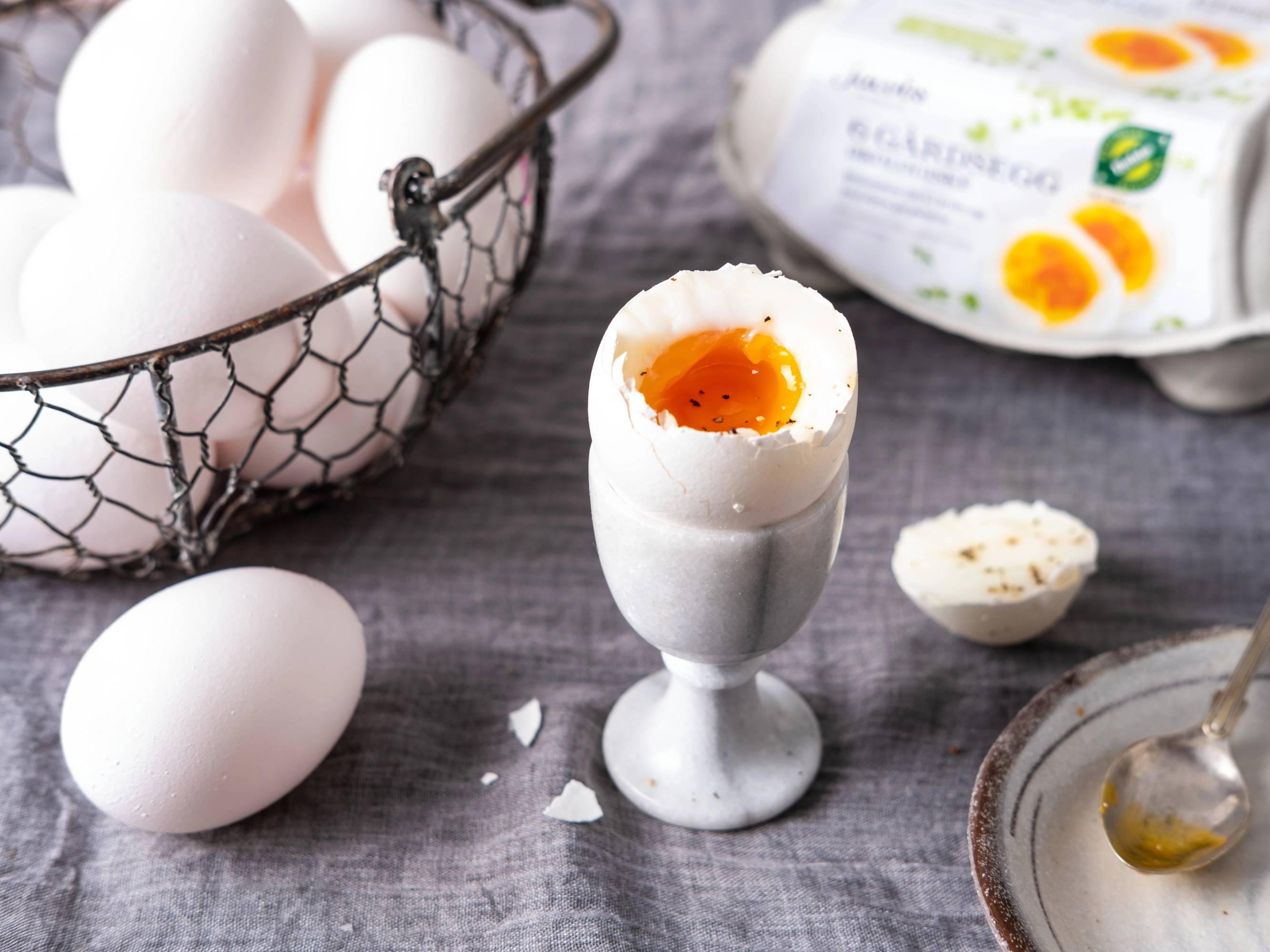 Bløtkokt egg i et eggeskall med en flytende eggeplomme, omgitt av andre egg og eggeskall på et bord.