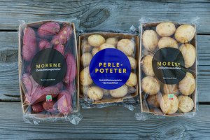 Bilde av tre pakker med poteter, to med lyse poteter og en med lilla poteter, på en treplate.