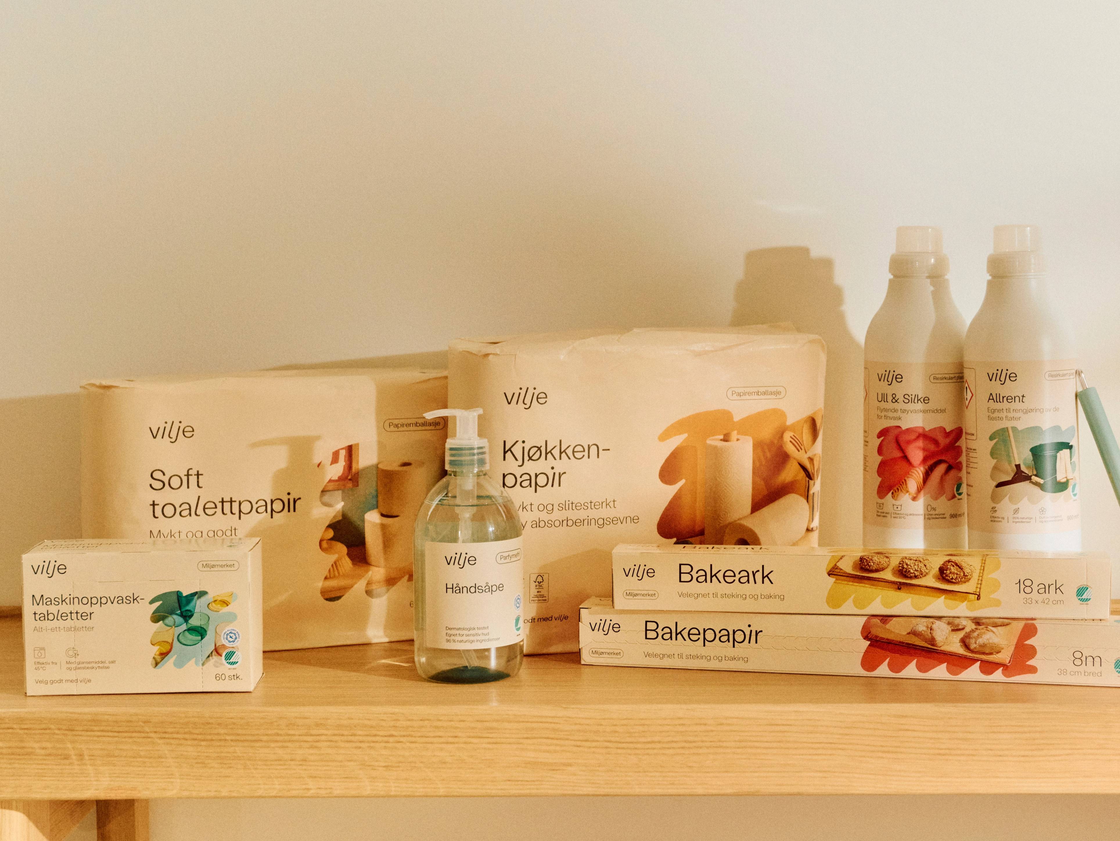 Ulike typer av papirprodukter og hygieneartikler på en hylle, inkludert toalettpapir, kjøkkenpapir og vaskemidler.