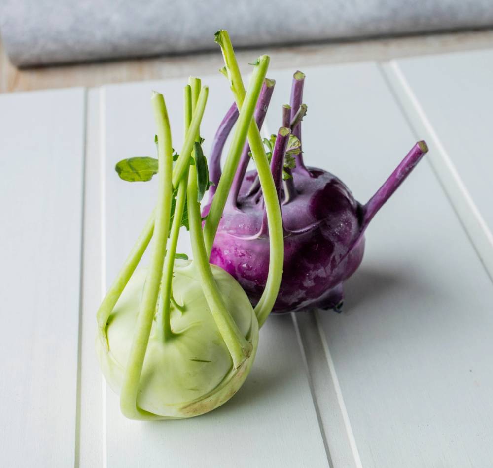 To kålrot med grønne og lilla stilker og blader på en hvit overflate.
