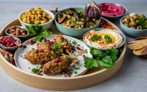 Varierte retter og småretter på et rundt serveringsfat med grønnsaker og dipper, inkludert kålrotstappe og oliven.