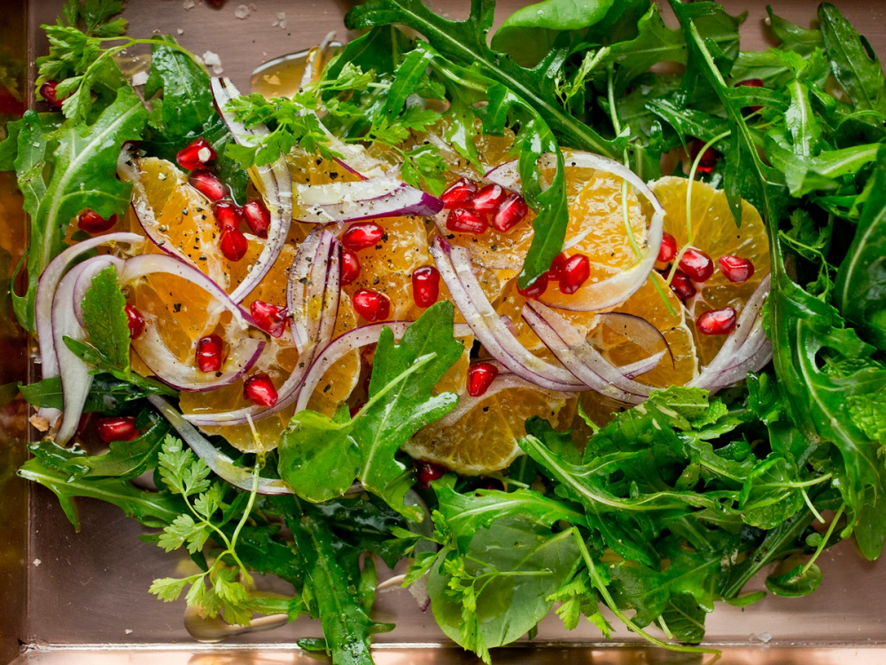 En salat med klementinbåter, granateplefrø, rødløk og grønn salat.