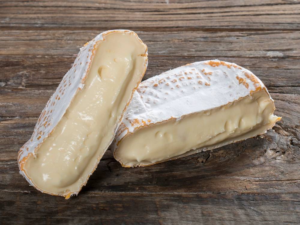 To ostesmørbrød med hvit ost på en treplate, ett av dem er delt i to.