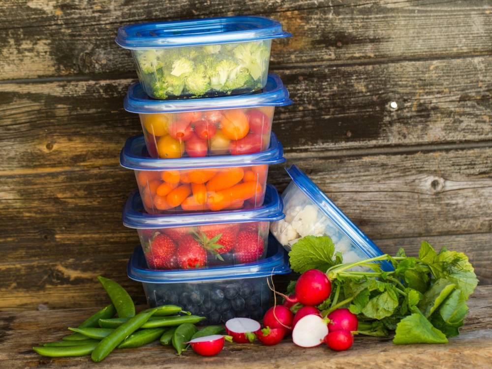 Fargede plastbokser med ulike typer frukt og grønnsaker, plassert på en trevegg.