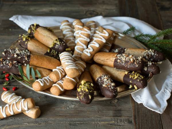 Kransekakestenger med sjokolade og pyntet med melis og non-stop, samlet på et fat med en hvit dukke under.