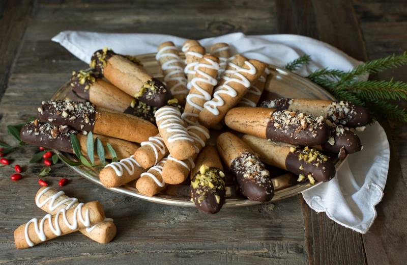 Kransekakestenger med sjokolade og pyntet med melis og non-stop, samlet på et fat med en hvit dukke under.