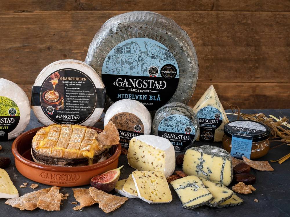 Et utvalg av oster og pålegg fra Gangstad, presentert på et bord med en treoverflate, inkludert blåmuggost, skinke og kjeks.