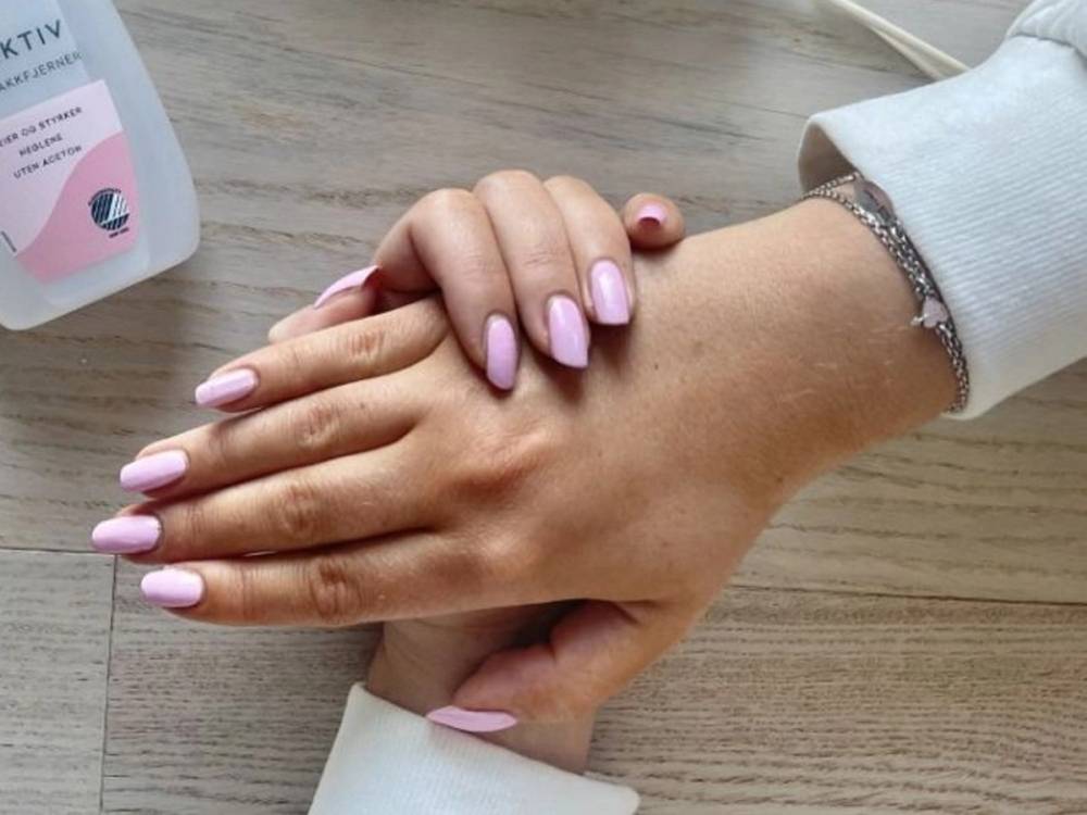 To hender med lyse lilla negler holder hverandre på et treverkbord.