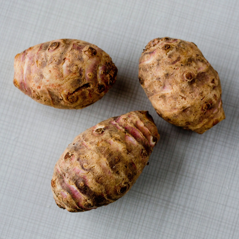 Tre jordskokk med rynkete, brune skinn på en lys bakgrunn.