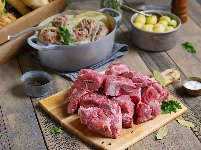 Kjøttstykker av fårekjøl på skjærebrett med tilbehør som poteter og krydder, klar til å bli tilberedt.