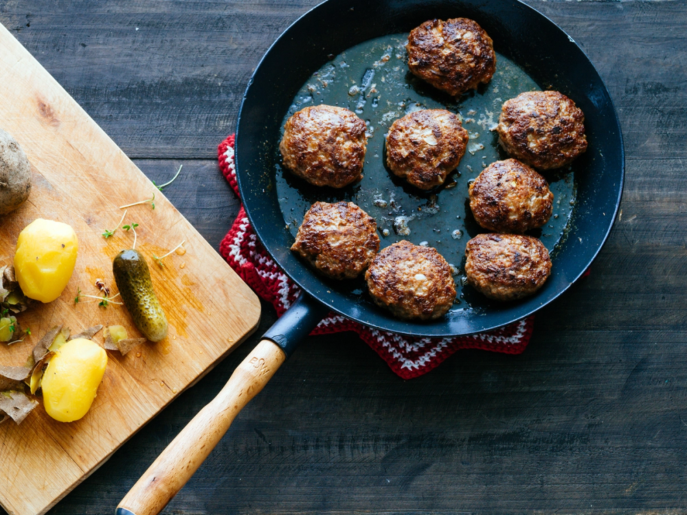 Kjøttboller stekes i en panne på et kjøkkenbord med en skjærefjøl og sitroner i bakgrunnen.