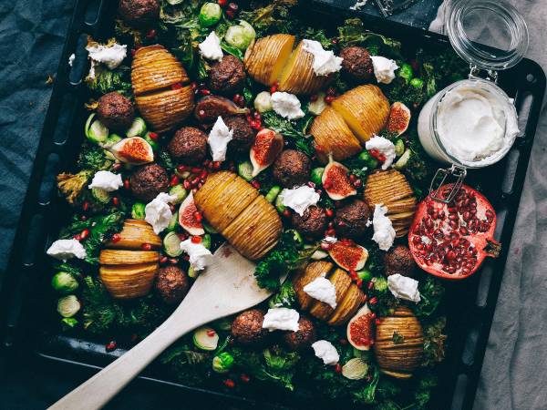 Lun vegetarisk salat med hasselbackpoteter, tomater, fetaost og grønt på en svart serveringsplate.
