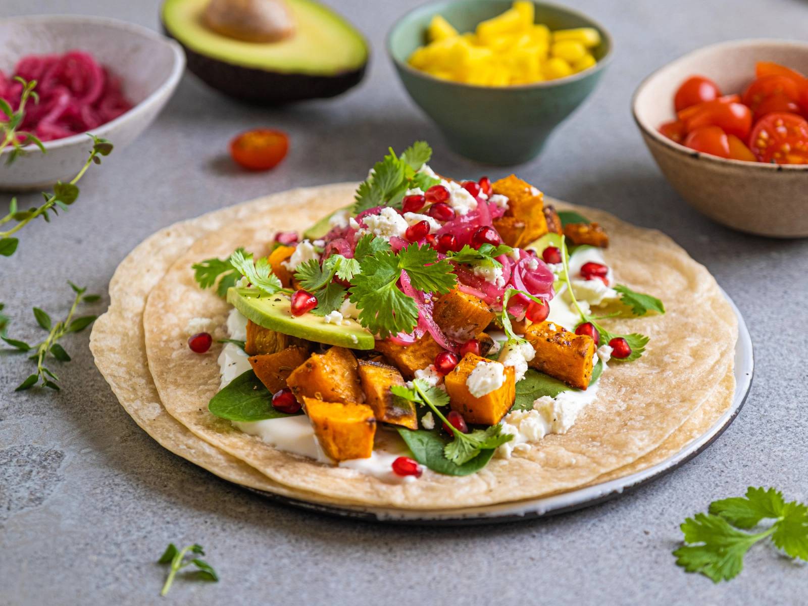 Vegetartaco med avokado, rødløk, koriander og tomater på en tortilla, omgitt av små boller med ulike grønnsaker og salsa.