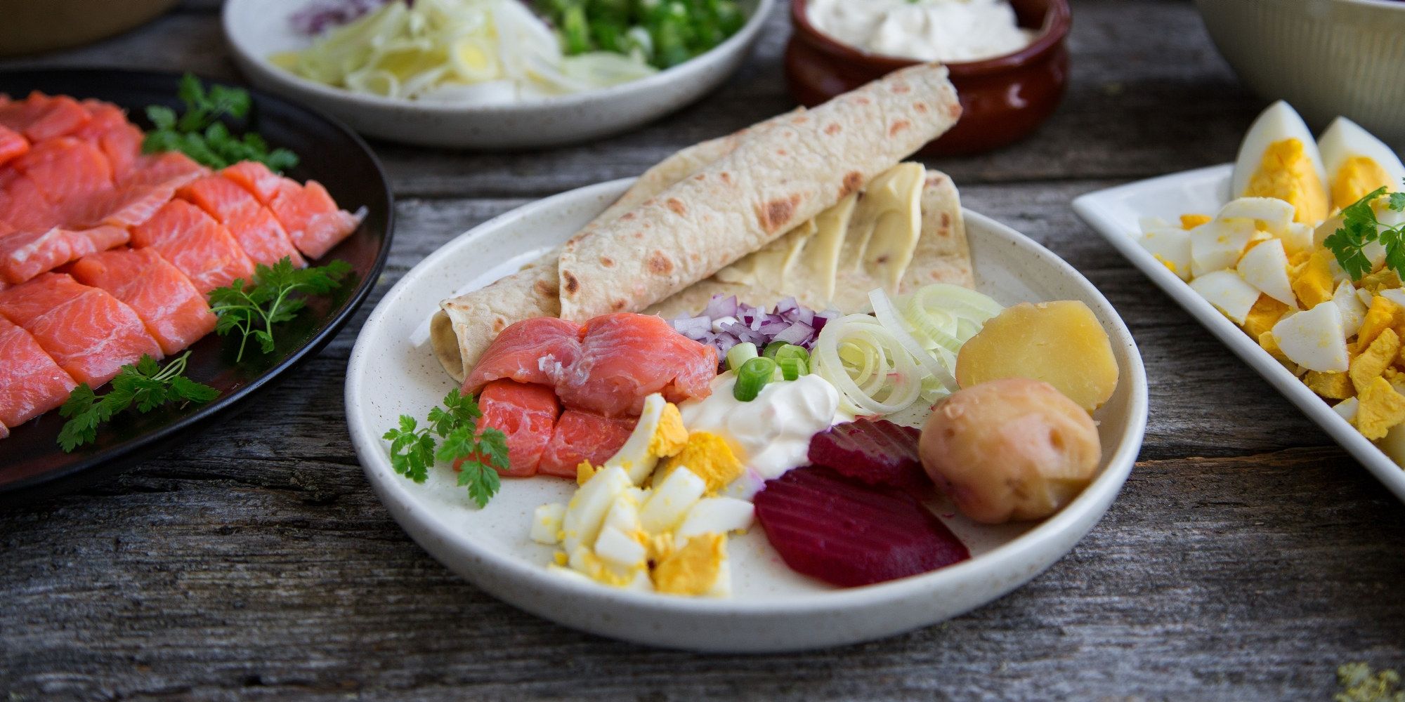 Tradisjonell rakfisk servert med lefse, løk, poteter og grønnsaker på et fat.