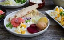 Tradisjonell rakfisk servert med lefse, løk, poteter og grønnsaker på et fat.