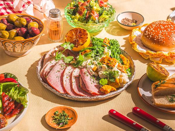 Et bord med en stor salat, skiver av roastbiff, en burger, frukt og diverse tilbehør på et festbord.