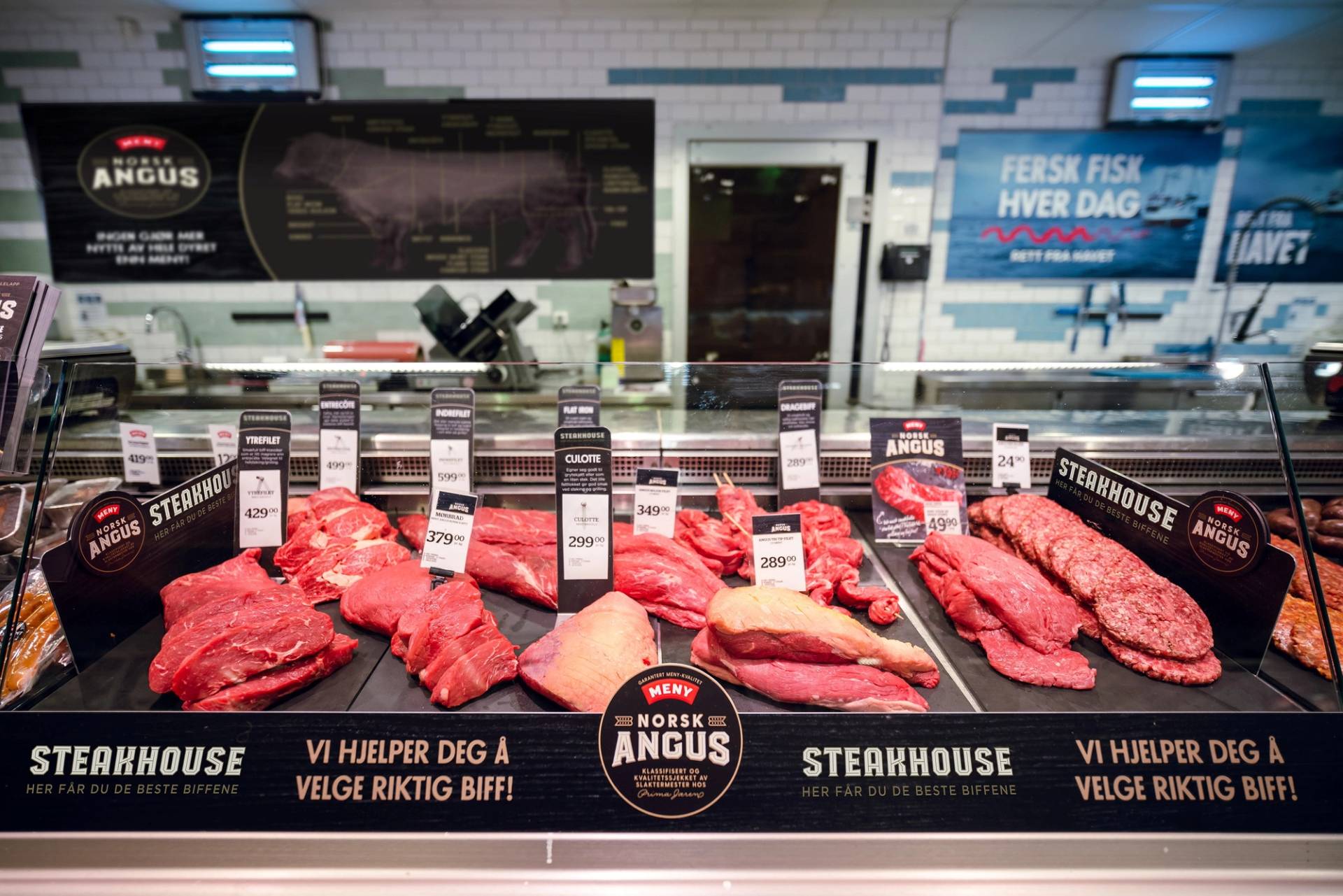 Ulike typer Angus-biff på en kjøttdisk i en butikk, med priser og informasjonsskilt over kjøttet.