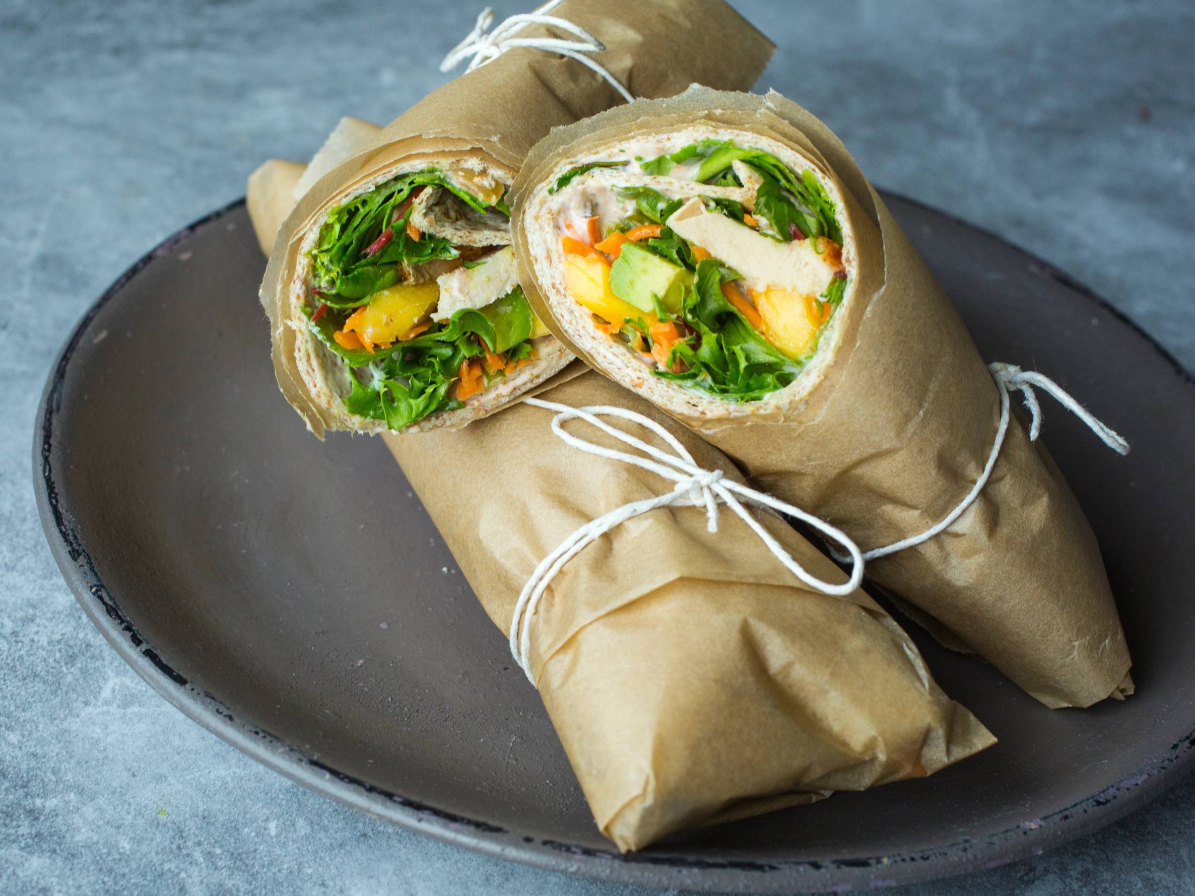 Grove wraps med kylling og mango på et svart fat, innpakket i papir og bundet med tau.