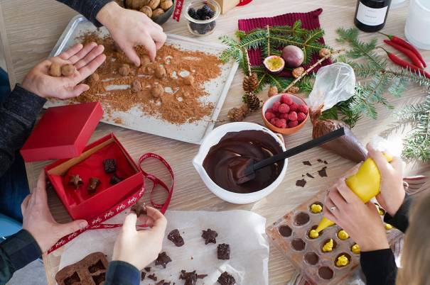 Personer lager julekonfekt med sjokolade, kakeformer og julepynt på bordet.