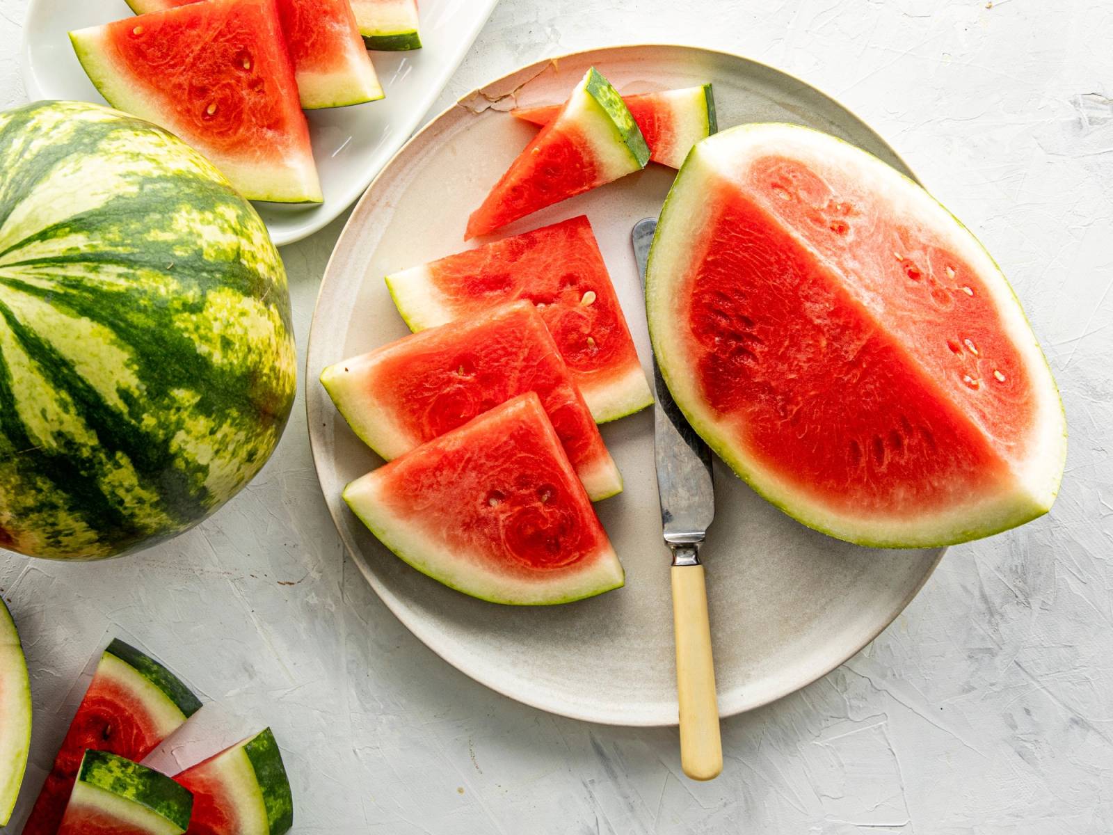 Skiver av vannmelon på en hvit tallerken med en hel vannmelon ved siden av, på et lyst bord.