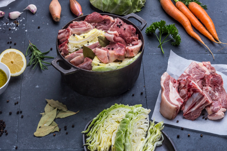 Fårikål-råvarer med kjøtt, kål, grønnsaker og krydder på et kjøkkenbord.