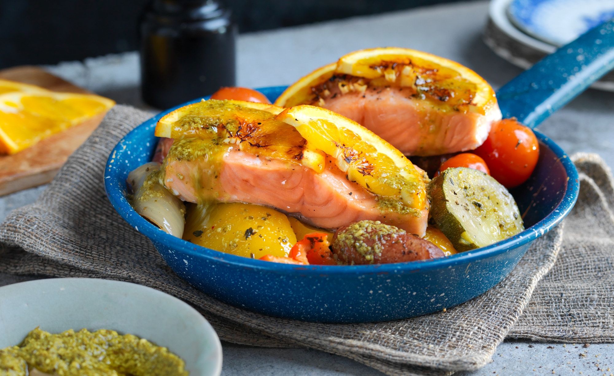 Laksefilet med ovnsbakte grønnsaker som poteter, gulrøtter og cherrytomater i en blå ildfast form.