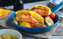 Laksefilet med ovnsbakte grønnsaker som poteter, gulrøtter og cherrytomater i en blå ildfast form.